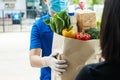Hand of food delivery service man wearing protection face mask holding fresh food set paper bag to customer at door home Royalty Free Stock Photo