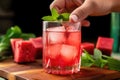 hand garnishing a glass of iced tea with wedge of watermelon
