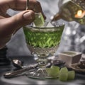 A hand gently dropping a sugar cube into a glass of absinthe with an ornate spoon3