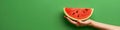 Hand gently holding a cut watermelon slice on a monochrome background