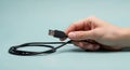 a hand gently holds a black usb cable with a standard type a connector on a light teal background Royalty Free Stock Photo