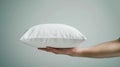 Hand gently holds and fluffs a white pillow against a clean, neutral background, emphasizing simplicity and balance in Royalty Free Stock Photo