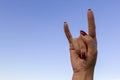 Hand gesturing rock & roll, heavy metal, devil horns gesture or I love you on blue sky background