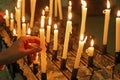 hand of girl that holding a lit candle in a church amidst a sea of flickering flames from the candles