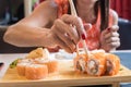 Hand of a girl in a red dress with red nails, takes fish sushi roll to chopsticks. Roll s stand on a wooden stand. Close Royalty Free Stock Photo