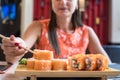 Hand of a girl in a red dress with red nails, takes fish sushi roll to chopsticks. Roll s stand on a wooden stand. Close Royalty Free Stock Photo