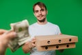 A hand gives money to a young man in a white T-shirt. The guy is holding boxes of pizza on a green background Royalty Free Stock Photo