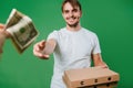 A hand gives money to a young man in a white T-shirt. The guy is holding boxes of pizza on a green background Royalty Free Stock Photo