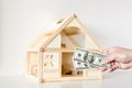 Hand giving one hundred us dollar banknotes. Wooden house model on background. Real estate investment.Bargain or deal concept Royalty Free Stock Photo