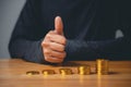 A hand giving a thumbs up in front of a growing stack of gold coins on a wooden Royalty Free Stock Photo