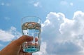 Hand with a glass water in front of blue and white sky