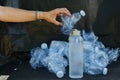 hand with glass water bottle in front of stack of plastic bottles, sustainable alternatives