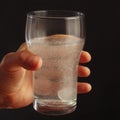 Hand with a glass of water and effervescent tablet from headache on dark background. Royalty Free Stock Photo