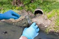 Hand in a glove with a bulb and a test tube against the background of a sewer pipe, dirty water. Pollution of ecology, environment Royalty Free Stock Photo