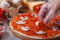 Hand in glove chef puts on a pizza base cherry tomatoes.