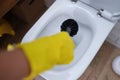 Hand in glove is cleaning toilet bowl with black brush closeup