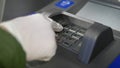 Hand in glove clicks on buttons of ATM, enters closeup password in bank, coronavirus in public place