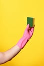 Hand with glove hoding scourer on yellow background Royalty Free Stock Photo