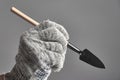 Hand in glove holding gardening spade like a pen on gray background