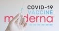 A hand with glove holding syringe in front of Moderna logo, one of the companies producing a Covid-19 Coronavirus vaccine.