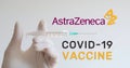 Hand with glove holds syringe next to AstraZeneca logo, one of the companies developing a Covid-19 Coronavirus vaccine.