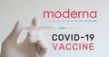 Hand with glove holds syringe next to Moderna logo, one of the companies developing a Covid-19 Coronavirus vaccine.