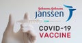 Hand with glove holds syringe next to Janssen, Johnson and Johnson logos, two of the companies developing a Covid-19 vaccine