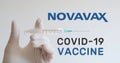 Hand with glove holds syringe next to Novavax logo, one of the companies developing a Covid-19 Coronavirus vaccine.