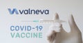 Hand with glove holds syringe next to Valneva logo, one of the companies developing a Covid-19 Coronavirus vaccine.