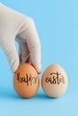Hand in glove keeping eggs with inscription HAPPY EASTER over blue background Royalty Free Stock Photo