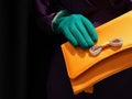 Hand with a green glove holding a bright yellow clutch bag