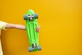 Hand with green penny board against yellow urban wall