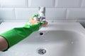 Hand in green rubber gloves clean sink in domestic bathroom yellow sponge and liquid foam detergent. Concept housework Royalty Free Stock Photo