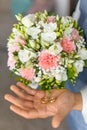 Hand of groom holding soft bridal bouquet of fresh flowers and wedding gold rings closeup. Elegant attribute and Royalty Free Stock Photo