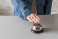 Hand of guest in a denim jacket ringing in silver bell. reception desk with copy space. Hotel service. Royalty Free Stock Photo