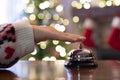 Hand of guest ringing reception bell on desk of guesthouse, hotel at christmas time. Color shining garland on christmas tree