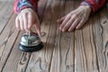 Hand of guest ringing in silver bell. on wooden rustic reception desk with copy space. Hotel, restaurant service. Selective focus. Royalty Free Stock Photo