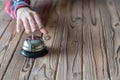 Hand of guest ringing in silver bell. on wooden rustic reception desk with copy space. Hotel service. Selective focus. Royalty Free Stock Photo