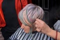 The hand of a hairdresser girl in a salon works with the hairstyle of a client of an adult woman with a colored, creative bob hair