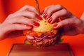 Hand half of the buns with sesame seeds on a big juicy Burger. Burger with cheese, vegetables and two cutlets. Red Royalty Free Stock Photo