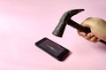 Hand with hammer destroying a smartphone on pink background