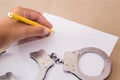 A hand in handcuffs sits at a table in front of a blank sheet of paper and a pen Royalty Free Stock Photo