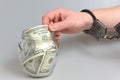 Hand in handcuffs taking money from glass jar on gray Royalty Free Stock Photo