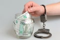 Hand in handcuffs taking money from glass jar on gray Royalty Free Stock Photo