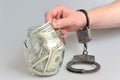 Hand in handcuffs taking money from glass jar on gray Royalty Free Stock Photo