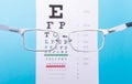 Hand-held glasses, view of the Snellen chart. Blue background Royalty Free Stock Photo