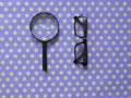 Hand-Held Reading Magnifier, Magnifying Glass, a Pair of Glasses with black frame on spotted dotty patterned background.