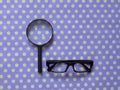 Hand-Held Reading Magnifier, Magnifying Glass, a Pair of Glasses with black frame on spotted dotty patterned background.