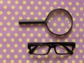 Hand-Held Reading Magnifier, Magnifying Glass, a Pair of Glasses with black frame on spotted dotty patterned background.