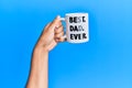 Hand of hispanic man holding best dad ever coffee cup over isolated blue background Royalty Free Stock Photo